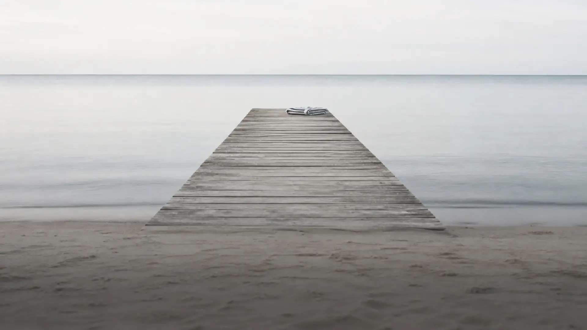 A wooden jetty reaching into mirror-flat water, a folded towel at the far end