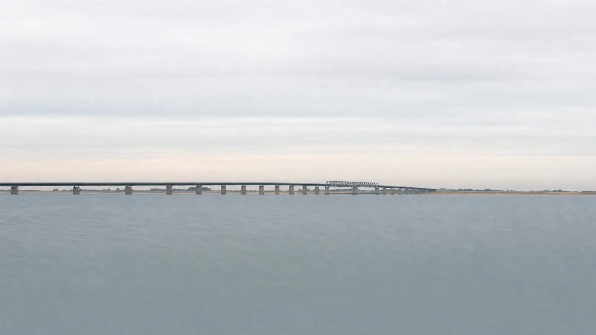 The Öresund Bridge stretching low across calm water towards the flat coastline